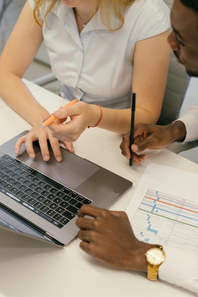 Two colleagues collaborating over a laptop and charts in an office setting.